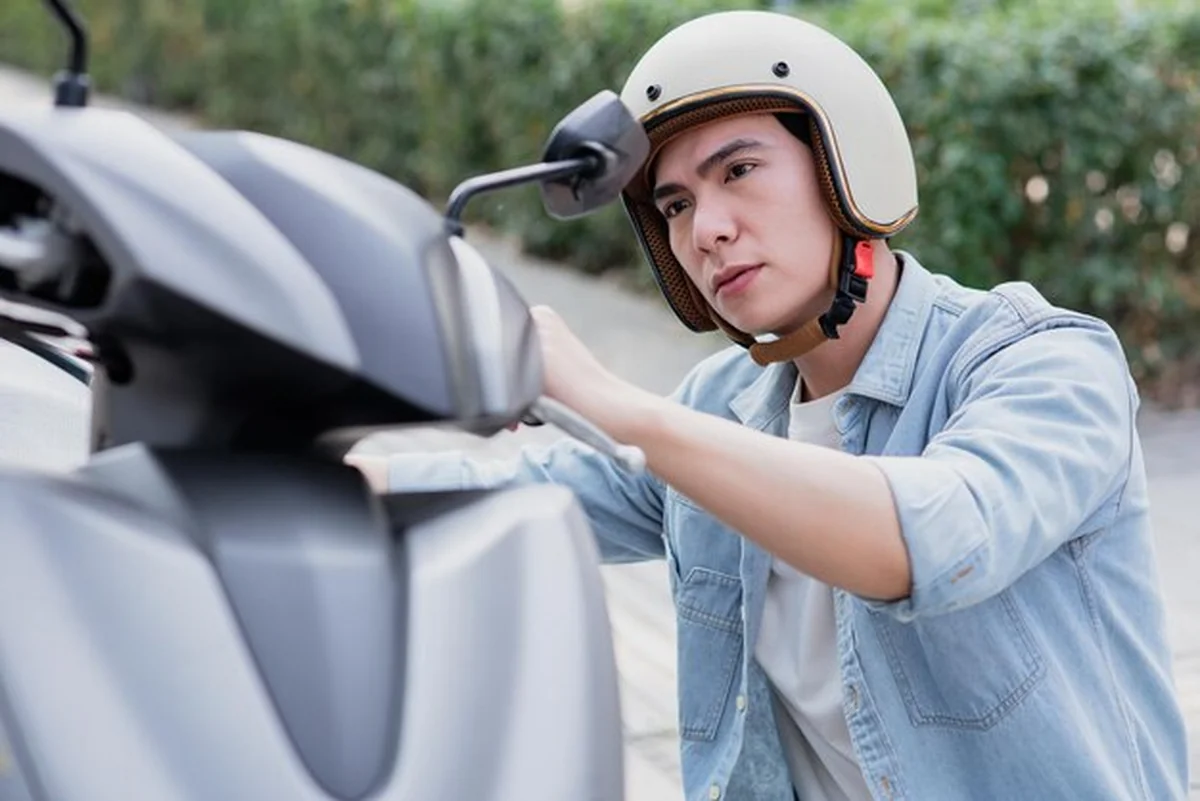 Młody mężczyzna w hełmie sprawdza skuter w dzielnicy miejskiej
