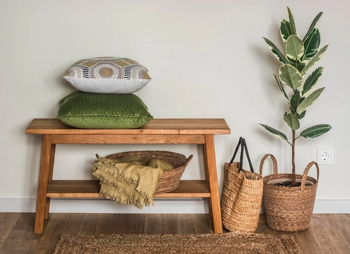 Przytulne wnętrze salonu z dębową ławą, poduszkami, koszem z kocami i fikusem w koszu
