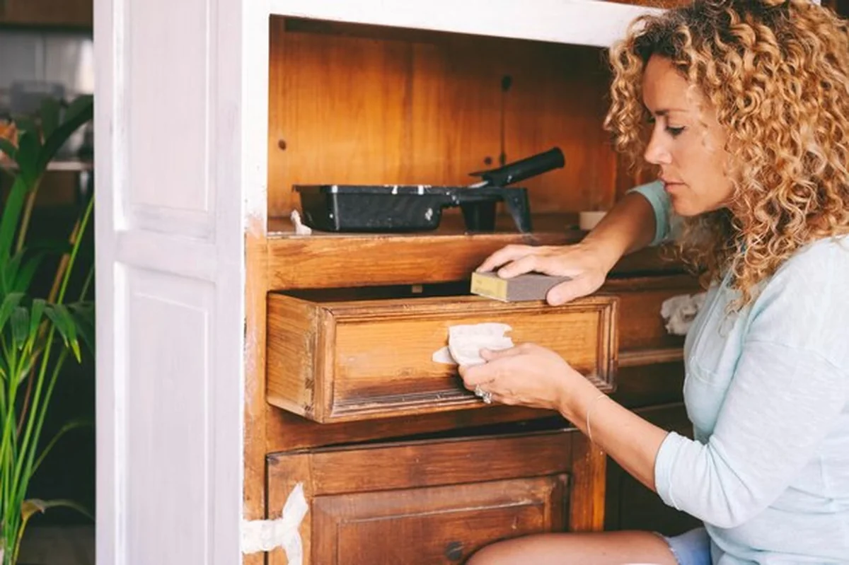 Kobieta odnawiająca drewnianą szafkę w domu