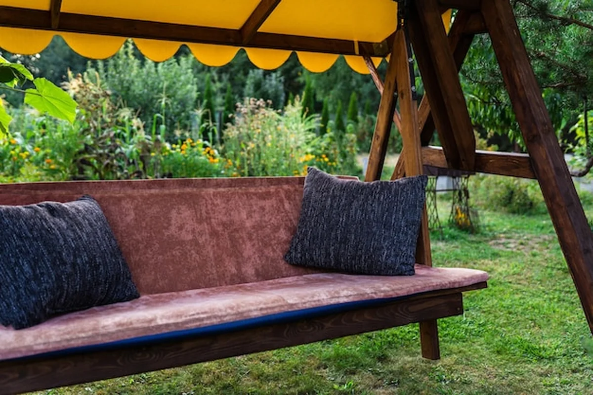 Duża drewniana huśtawka z baldachimem w ogrodzie obok domu