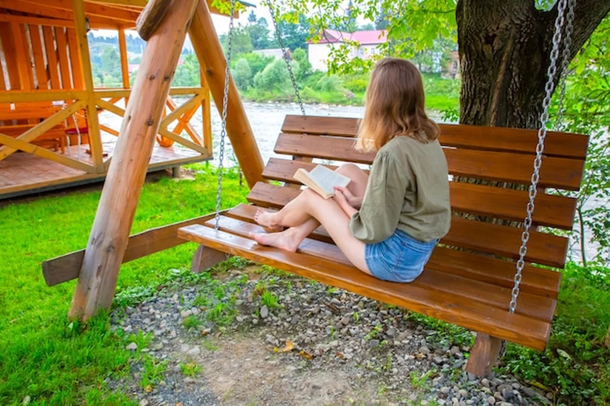 Kobieta czytająca książkę na drewnianej ławce w ogrodzie