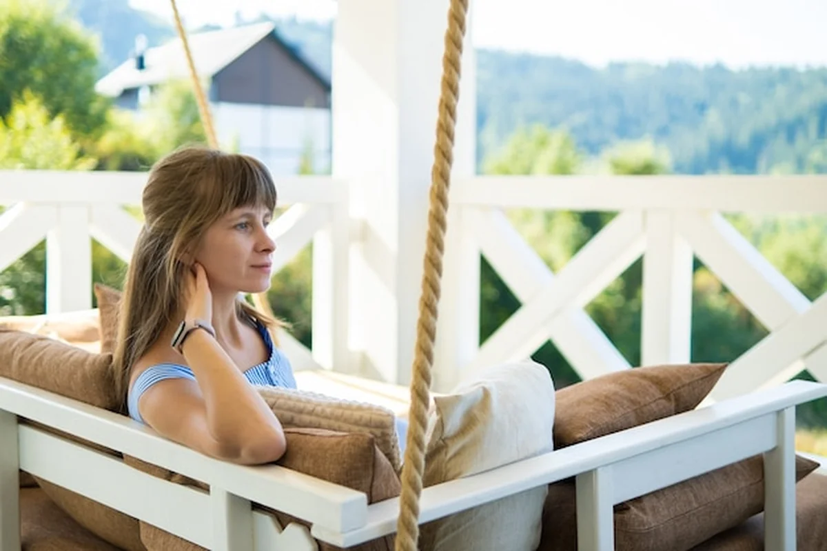 Młoda brunetka na tarasie z miękkimi poduszkami, letnia przyroda w tle