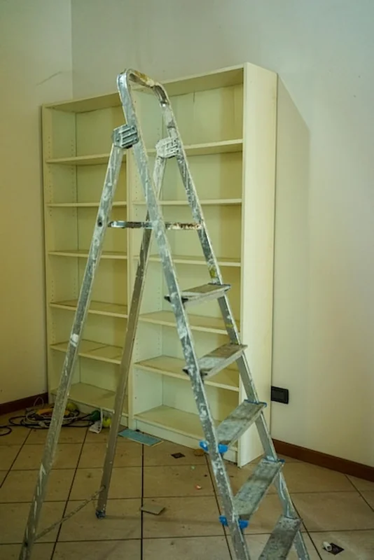 Aluminiowa drabina przed białą półką z książkami podczas renowacji