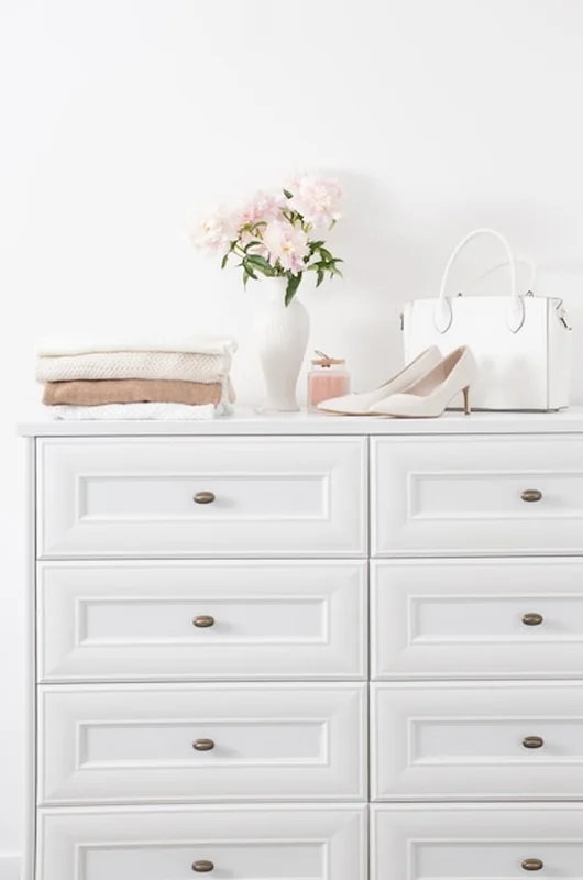 Biała komoda z ubraniami i kwiatami w białym pokoju