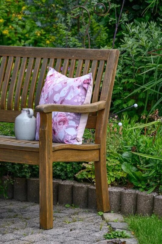 Drewniana ławka z kwiatową poduszką i dzbankiem w ogrodowej scenerii