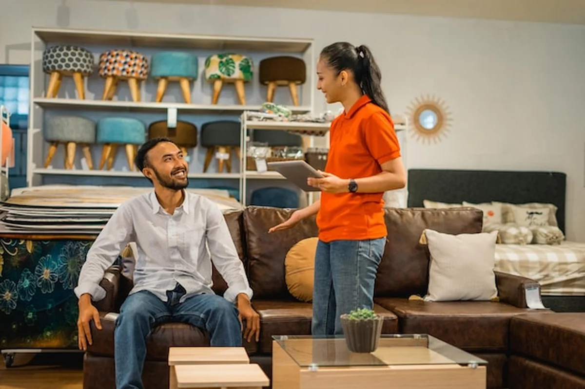 Klient płci męskiej na sofie, pracownica sklepu z tabletem w meblach