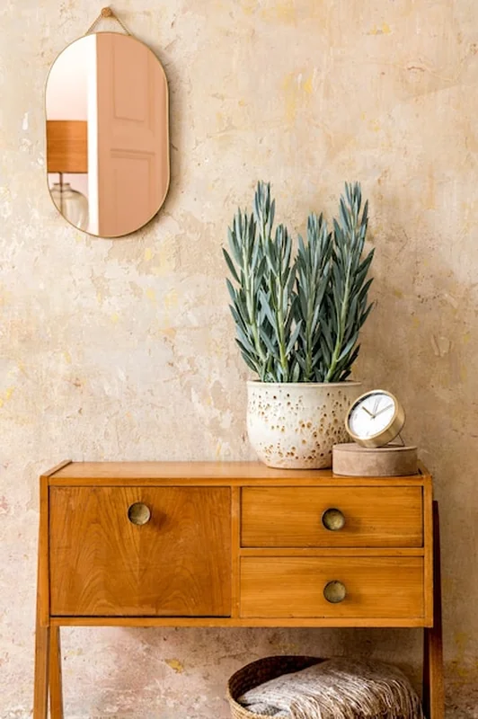 Stylowa kompozycja wnętrza salonu z drewnianą komodą vintage, złotym lustrem, rośliną i rattanowym koszem