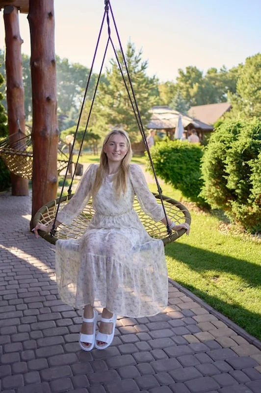 Młoda blondynka w pastelowej sukience lecąca w hamaku