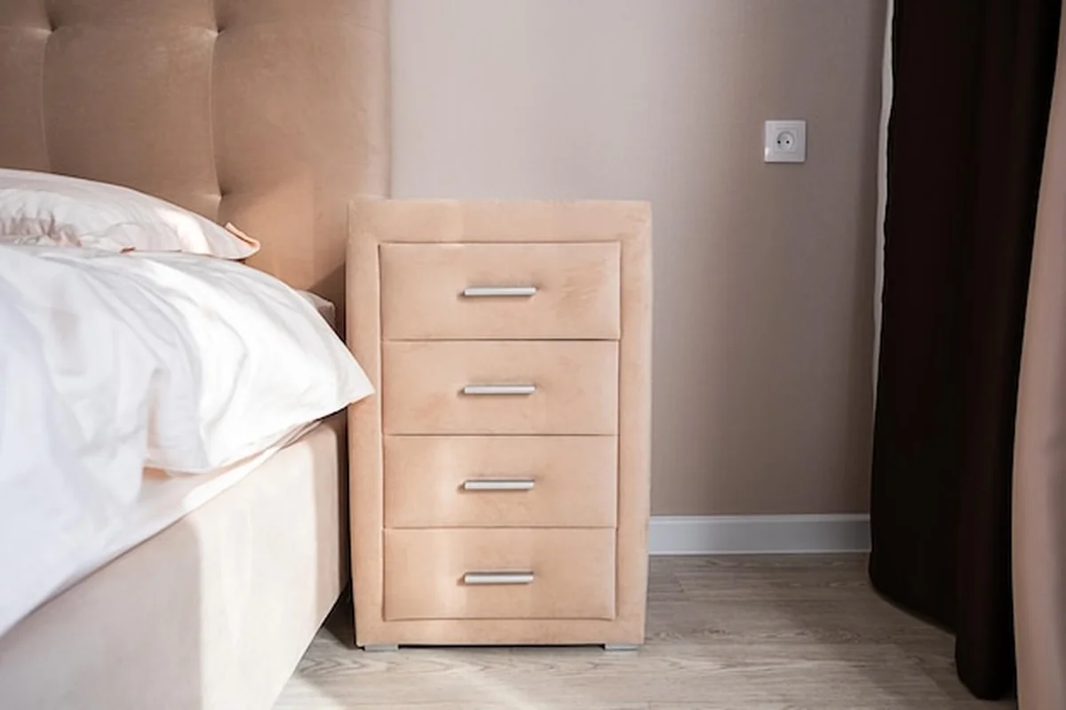 Beżowa szafka z czterema szufladami obok łóżka w naturalnym świetle