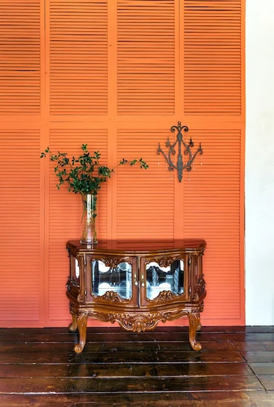 Stylowa aranżacja wnętrza salonu z komodą drewnianą w stylu retro i pomarańczowymi ścianami