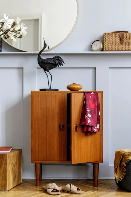 Nowoczesne wnętrze z designerską drewnianą komodą, lustrem, zegarem, rośliną, ubraniami i akcesoriami w salonie