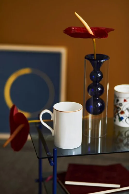 Stylowa kompozycja w nowoczesnym wnętrzu salonu z designerskim stolikiem kawowym, kubkiem, książką i czerwonym kwiatem