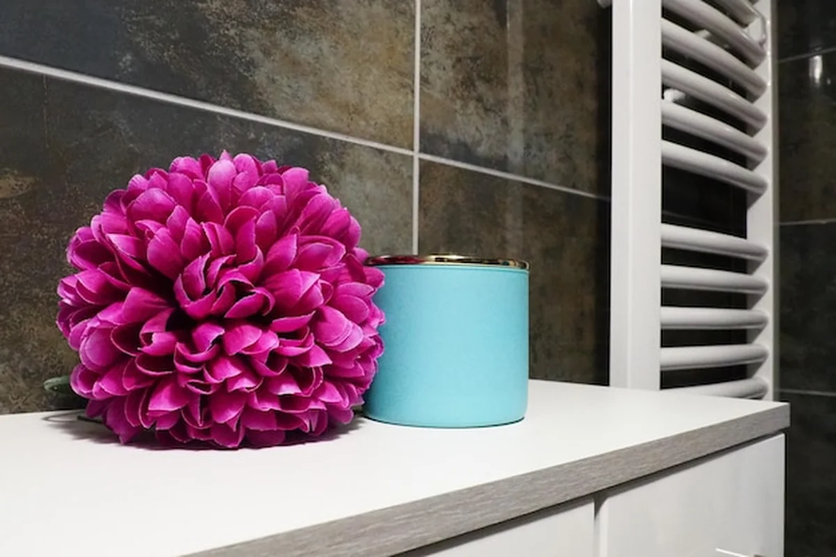 Niebieski słoik kremu i różowy kwiat na półce, czarne płytki ścienne w nowoczesnej łazience