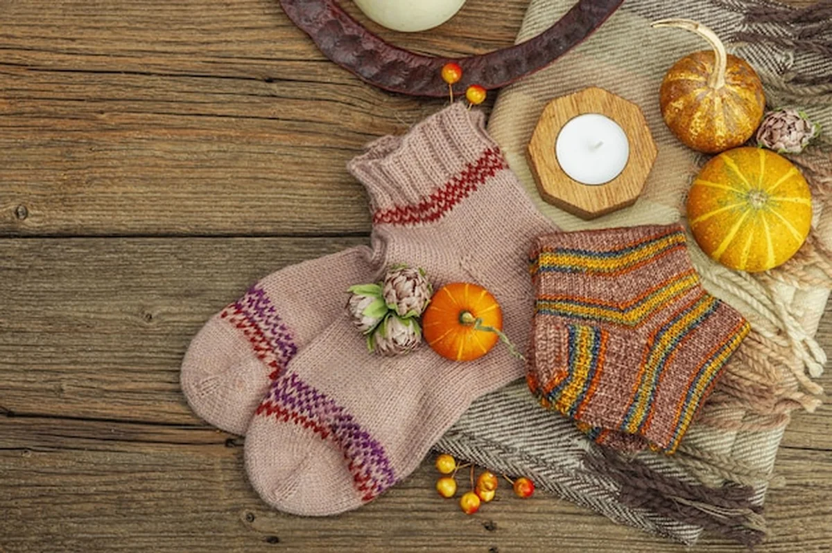 Jesienna kompozycja z szalikiem, skarpetkami, świecami, dynią i drewnianym tłem