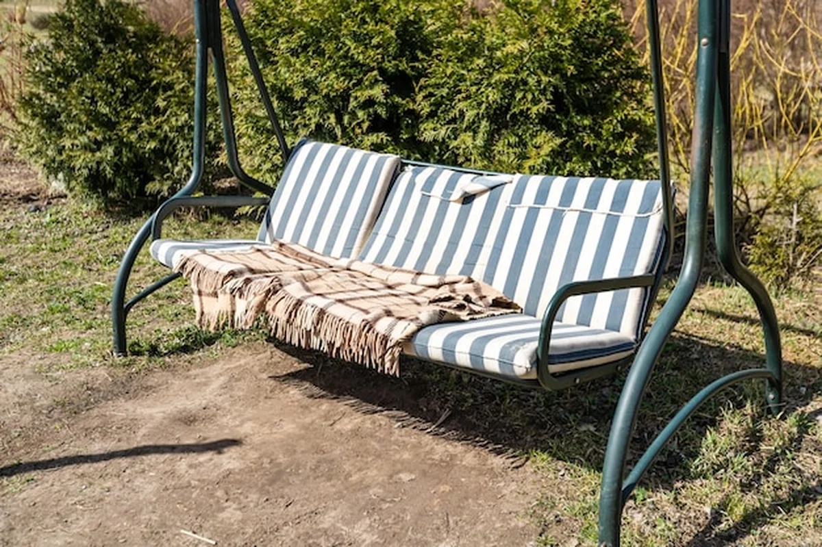 Ławka huśtawka w bujnym ogrodzie z gałęzią drzewa