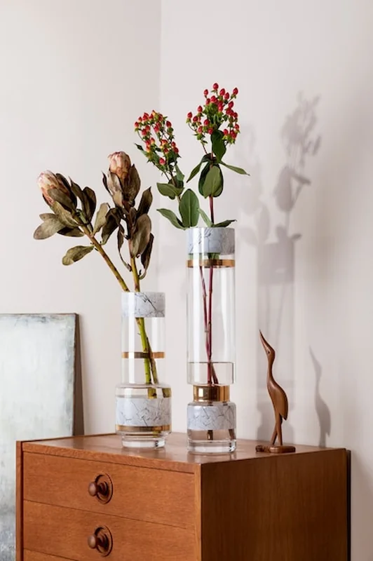 Kwiatowa kompozycja w nowoczesnych wazonach na komodzie retro z eleganckimi dodatkami